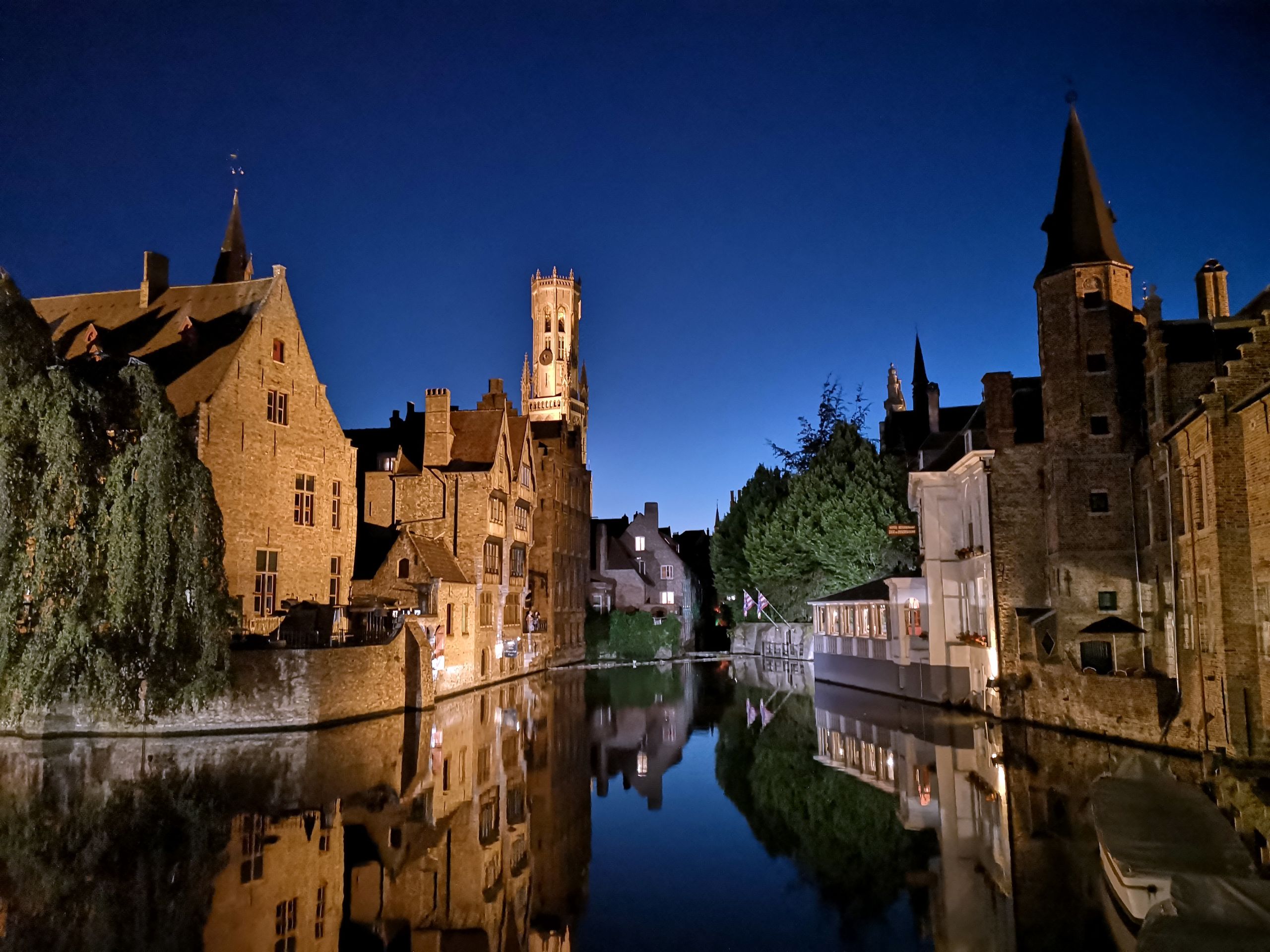 Veduta notturna del canale di Bruges, con edifici illuminati e riflessi sull’acqua.